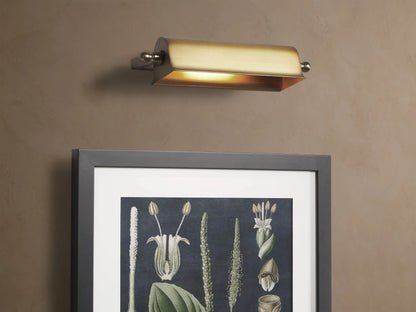 Antiqued brass Tremont Picture Light Sconce, horizontally mounted on a light beige textured wall, with finials.