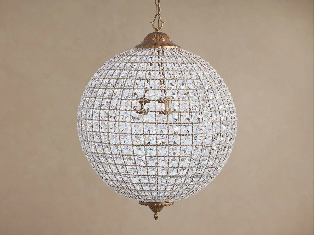 Poppy Chandelier, a glowing spherical fixture of clear multifaceted crystals on an antiqued brass frame, suspended.