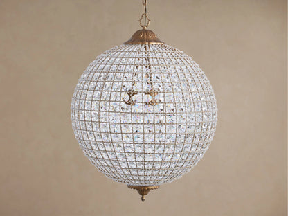 Poppy Chandelier, a glowing spherical fixture of clear multifaceted crystals on an antiqued brass frame, suspended.