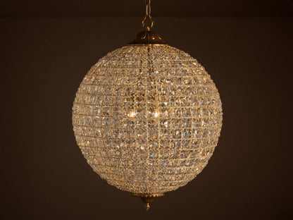 Poppy Chandelier, a glowing spherical fixture of clear multifaceted crystals on an antiqued brass frame, suspended.