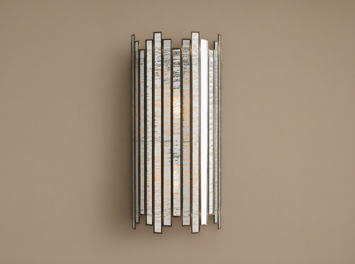 Laila Sconce: vertical antique copper frame with rectangular antiqued mirrored-glass panels, glowing softly against a beige wall.