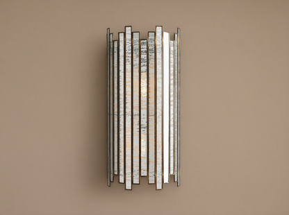 Laila Sconce: vertical antique copper frame with rectangular antiqued mirrored-glass panels, glowing softly against a beige wall.