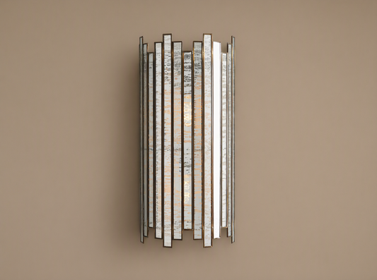 Laila Sconce: vertical antique copper frame with rectangular antiqued mirrored-glass panels, glowing softly against a beige wall.