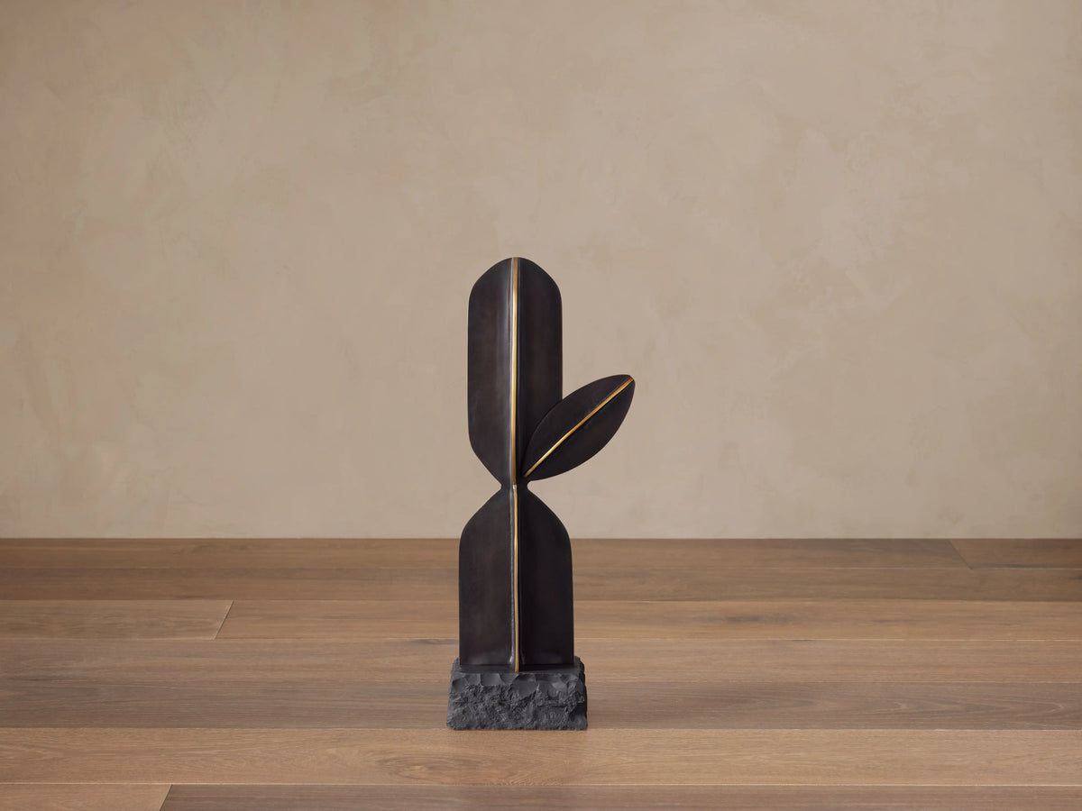 Modern black aluminum Cactus Sculpture with antiqued brass lines, on a textured black base, standing on a wood floor.