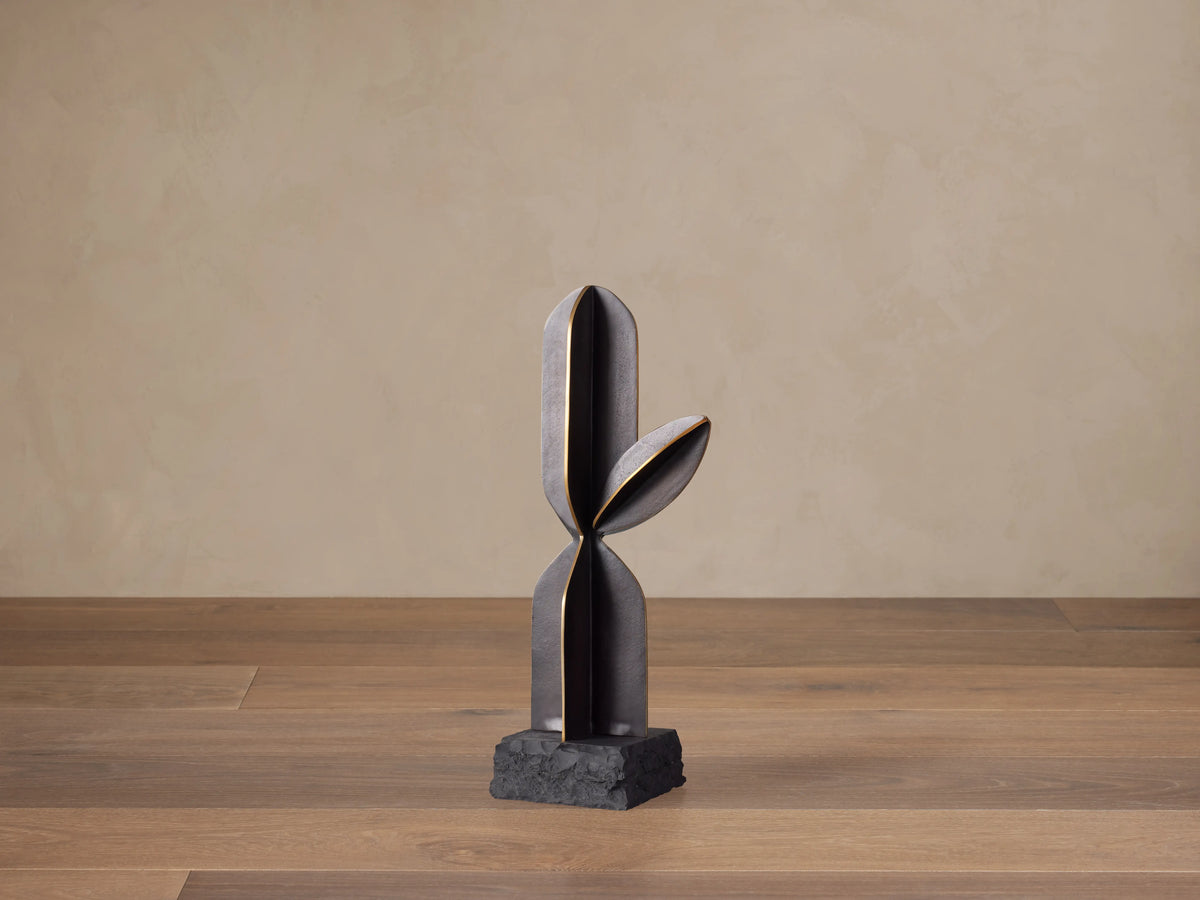 Modern black aluminum Cactus Sculpture with antiqued brass lines, on a textured black base, standing on a wood floor.