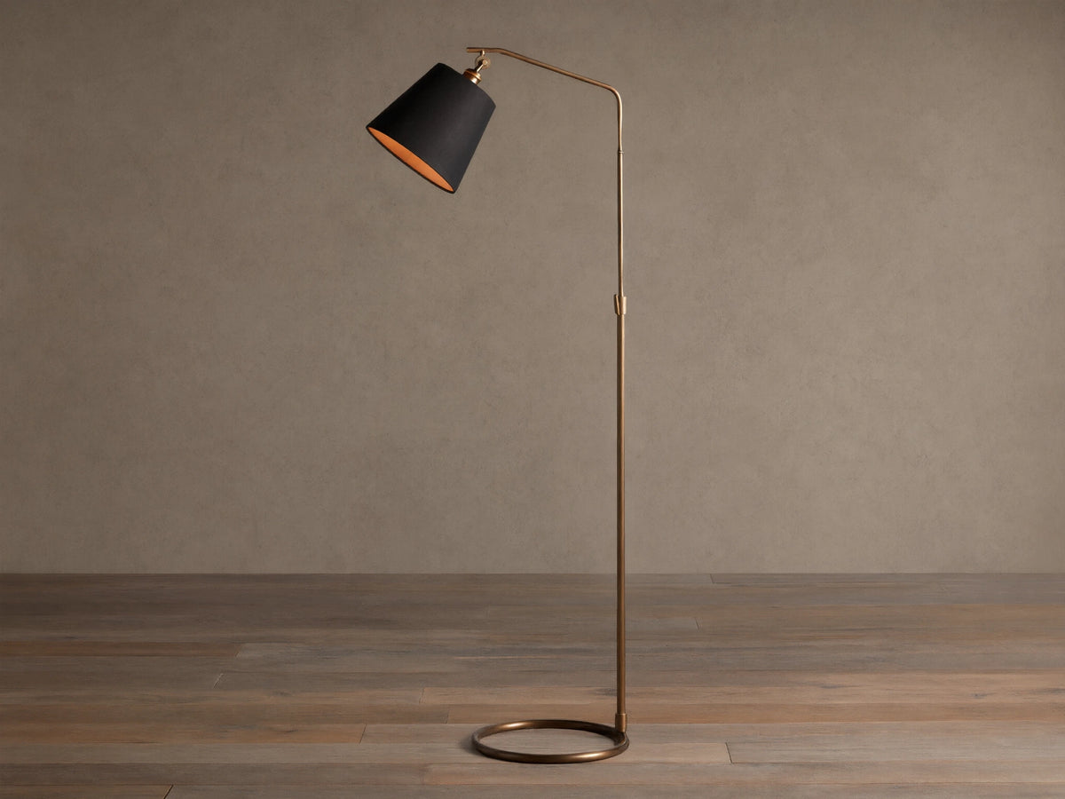 Kellen Antiqued Brass Floor Lamp, slender frame, black fabric shade with warm interior, round base on wooden floor.