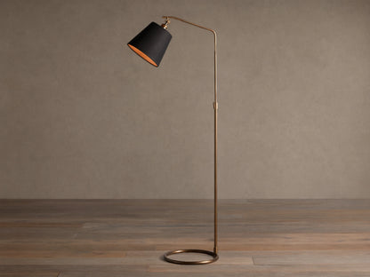 Kellen Antiqued Brass Floor Lamp, slender frame, black fabric shade with warm interior, round base on wooden floor.