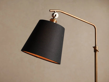 Kellen Antiqued Brass Floor Lamp with a slender, curved antiqued brass stand and black conical shade, warm interior.