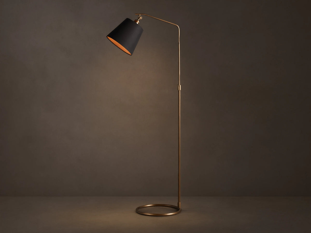 Kellen Antiqued Brass Floor Lamp, slender frame, black fabric shade with warm interior, round base on wooden floor.