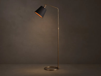 Kellen Antiqued Brass Floor Lamp, slender frame, black fabric shade with warm interior, round base on wooden floor.