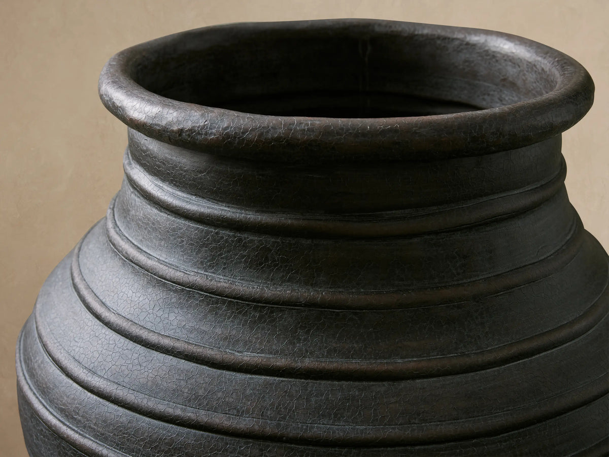 Dark gray, textured Artem Outdoor Planter with horizontal ridges, filled with pink flowers on a console table.