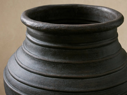 Dark gray, textured Artem Outdoor Planter with horizontal ridges, filled with pink flowers on a console table.