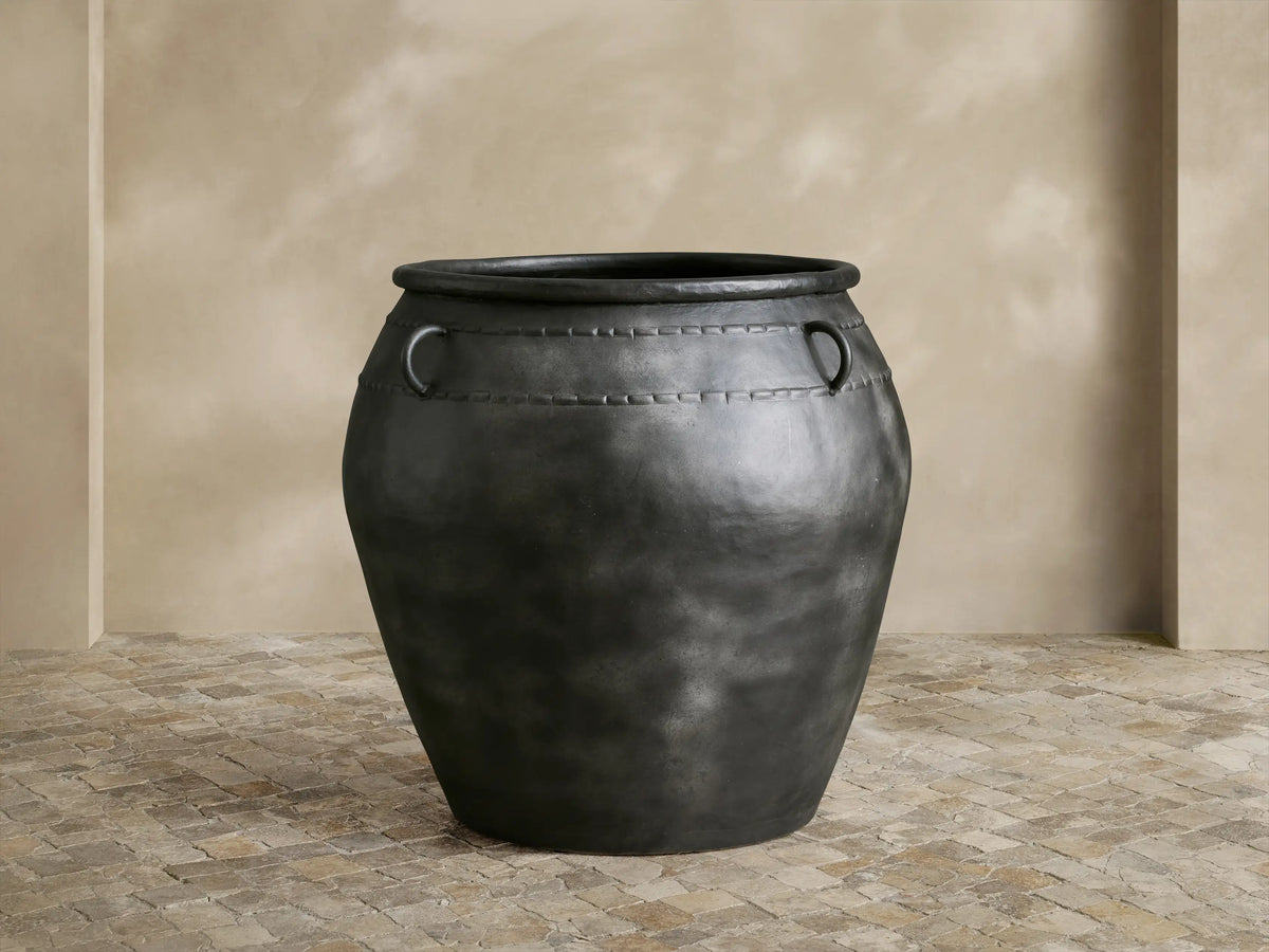 Ilya Outdoor Planter: large, dark charcoal aged metal planter with two ring handles and decorative stitching, on stone floor.