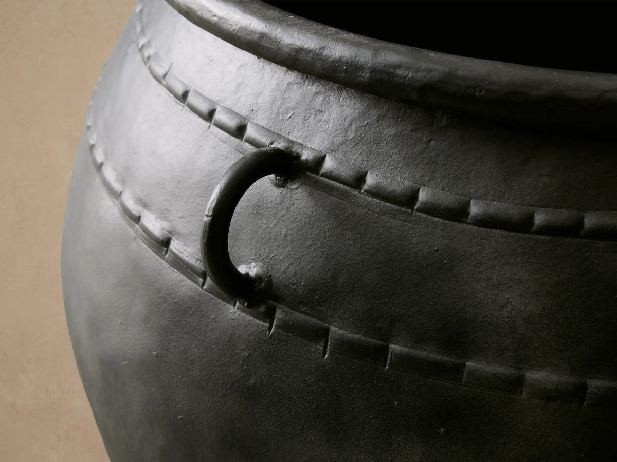 Ilya Outdoor Planter: large, dark charcoal aged metal planter with two ring handles and decorative stitching, on stone floor.
