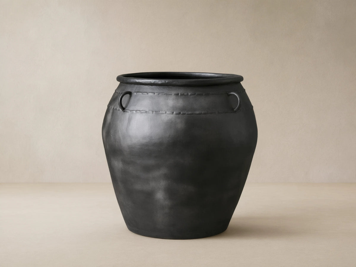 Ilya Outdoor Planter: large, dark charcoal aged metal planter with two ring handles and decorative stitching, on stone floor.