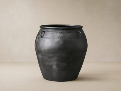 Ilya Outdoor Planter: large, dark charcoal aged metal planter with two ring handles and decorative stitching, on stone floor.