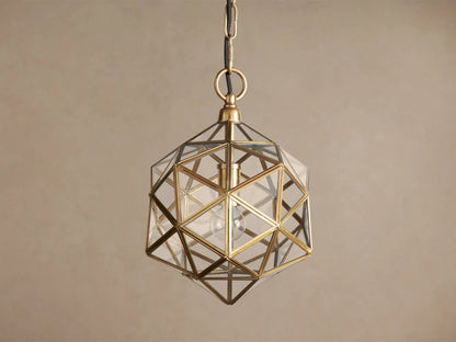 Illuminated Eliana Lantern Pendant with geometric brass frame and clear glass panels, hanging from a chain against a warm wall.