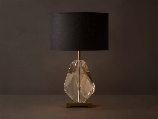 Lola Teardrop Table Lamp with black drum shade, clear faceted crystal base, and brass accents, on a wooden table.