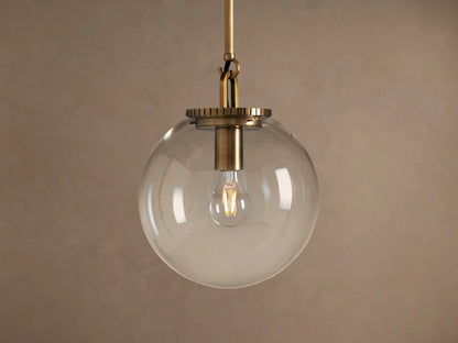 Wescott Globe Pendant: Brass-finished rod and hardware holding a clear glass globe with a filament bulb inside, against a plain wall.