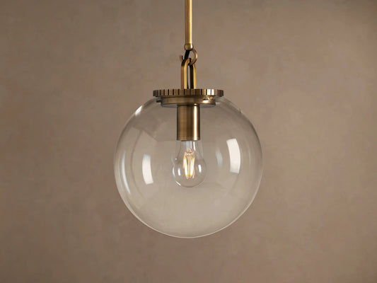 Wescott Globe Pendant: Brass-finished rod and hardware holding a clear glass globe with a filament bulb inside, against a plain wall.