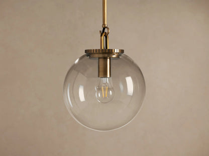 Wescott Globe Pendant: Brass-finished rod and hardware holding a clear glass globe with a filament bulb inside, against a plain wall.