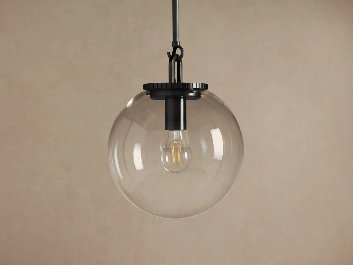 Wescott Globe Pendant with Rod, featuring a clear glass globe, dark bronze rod, and a warm glowing bulb against a taupe wall.
