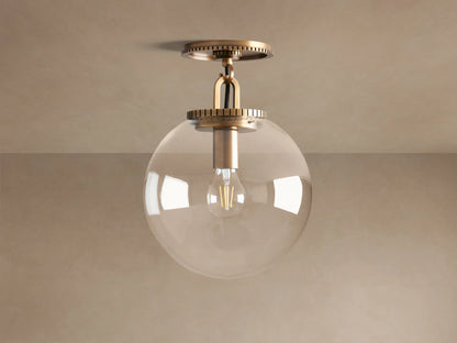 Wescott Globe Flush Mount with a clear glass globe shade, brass hardware, mounted on a ceiling against a neutral wall.