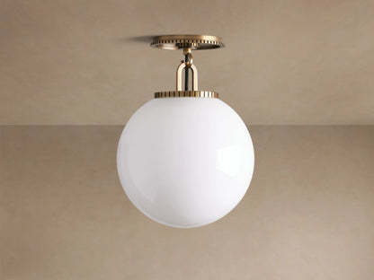 Wescott Globe Flush Mount: Brass fixture with ribbed detail, holding a large white opal glass globe on a tan ceiling.