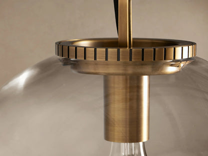Wescott Globe Pendant. Clear glass globe, brass hardware & chain, light bulb visible inside, hanging against beige wall.