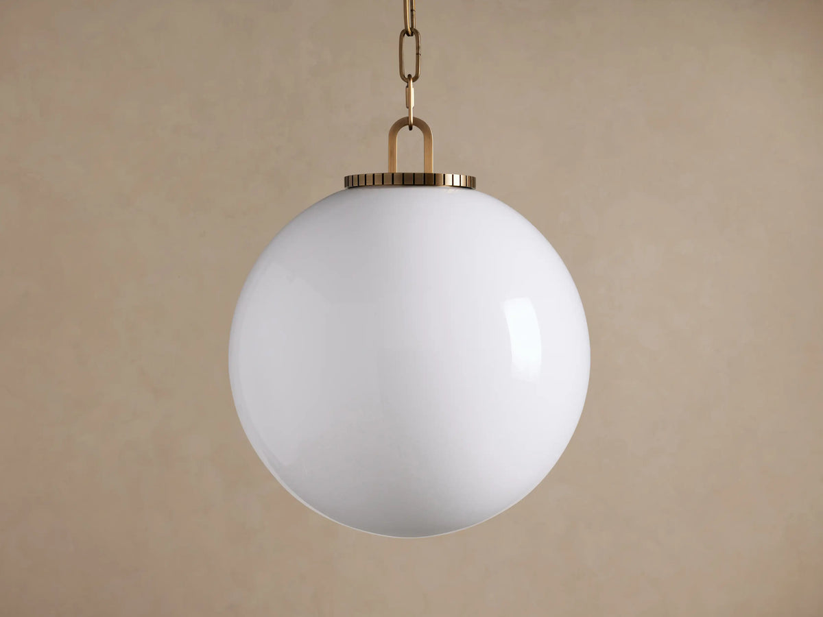 Wescott Globe Pendant. Large, illuminated milky white glass globe hangs from a brass chain & fitting, brown background.