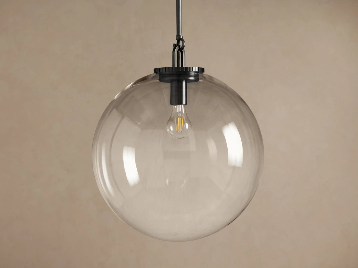 Wescott Globe Pendant: clear glass sphere shade, dark metal rod, and visible vintage filament bulb against a light brown wall.