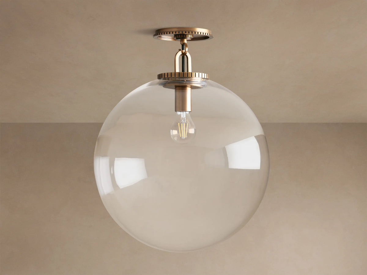 Wescott Globe Flush Mount with clear glass globe, exposed Edison bulb, and brass hardware, mounted on a beige ceiling.