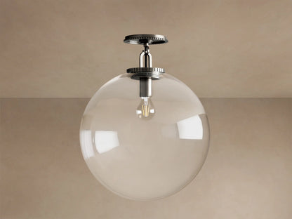 Wescott Globe Flush Mount: clear glass globe, lit Edison bulb, dark bronze mount, metallic stem on a beige ceiling.