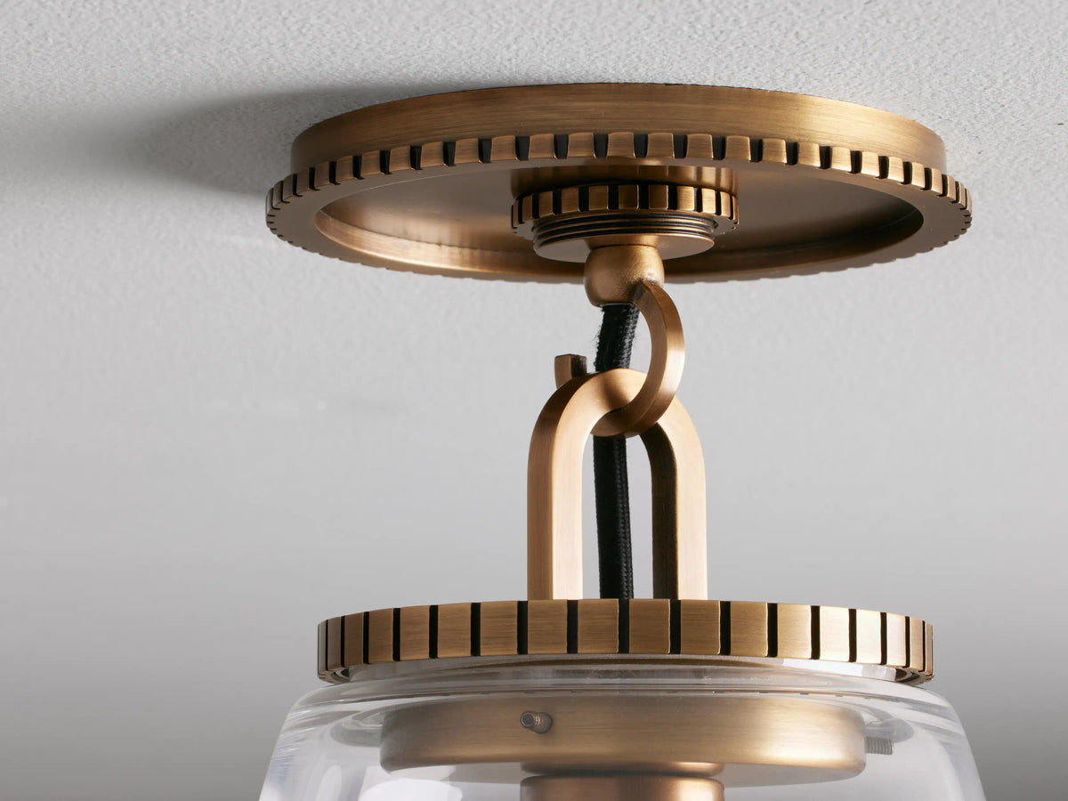 Clear glass cone shade flush mount light with brass finished base, mounted on the ceiling. Bulb visible inside.
