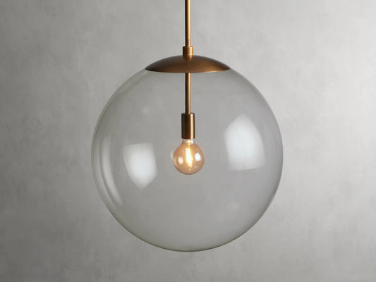 A clear glass globe pendant with a brass finish rod and fixture, showcasing a visible bulb inside, hung against a plain background.