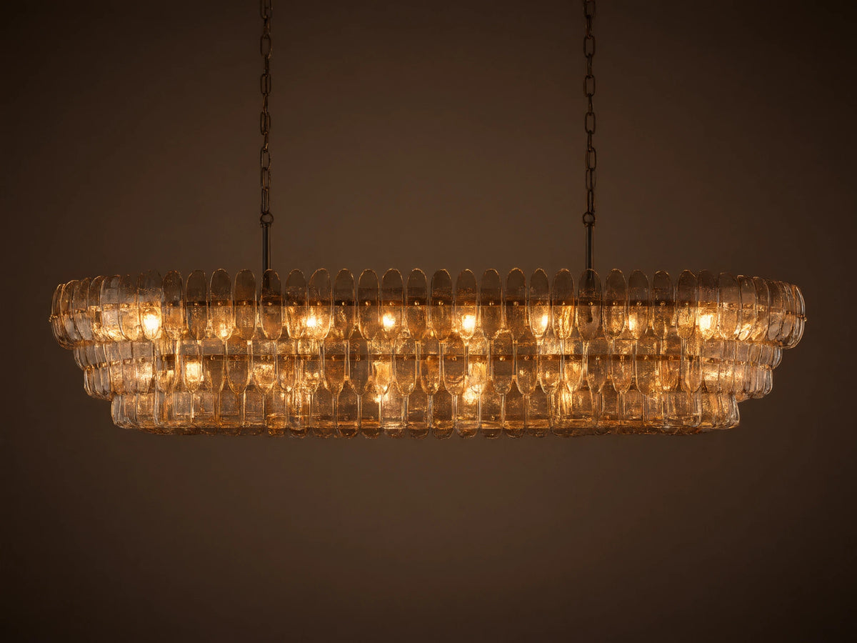 Ghiaccio Oval Chandelier: clear textured glass in tiered wavy segments, suspended by dark chains, with a soft inner glow.