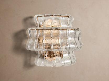 Ghiaccio Sconce: a layered wall light featuring clear, wavy textured glass and a warm, gold-toned frame, illuminated on a wall.