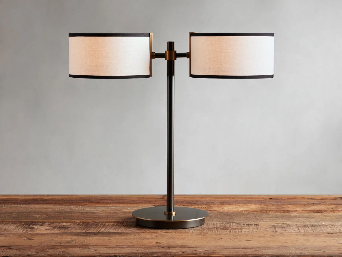 Daphne 2-Light Table Lamp with black-finished base and two white linen shades with black trim on a wooden surface.