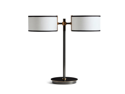 Two-light table lamp with bronze base, featuring dual white linen shades with black trim. Positioned on a wooden surface.