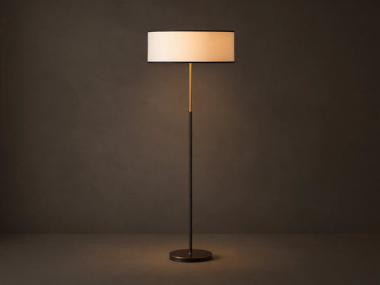 Daphne Floor Lamp with a slim bronze-finished stand, round white linen shade with black trim, wooden floor background.
