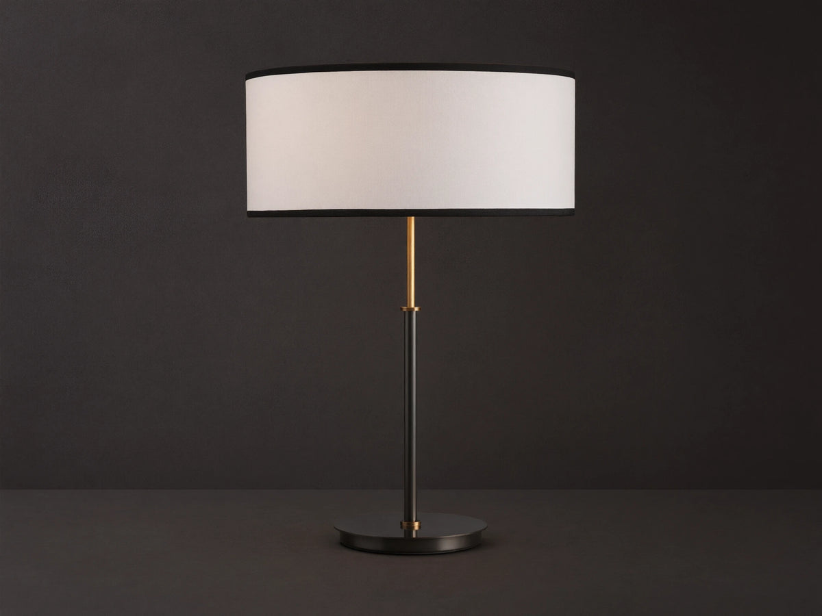 Daphne Table Lamp with white linen shade, black trim, dark bronze finish, and brass accent, on a wooden table.