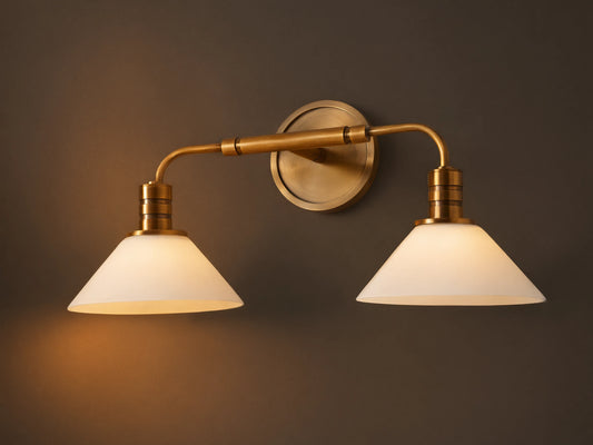Theron Double Sconce: A brass-finished wall light with two horizontal arms holding conical milk glass shades on a grey wall.