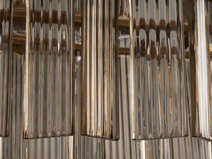 Close-up of Delsie Oval Chandelier's clear, ribbed glass rods hanging vertically, with warm brass-toned metal in the background.