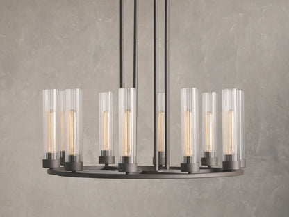 Andreas 10-Light Round Chandelier with a bronzed steel frame, featuring ten vertical, tubular clear glass shades. Mounted against a textured grey wall.