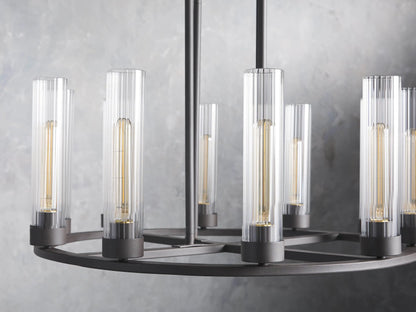 Andreas 10-Light Round Chandelier with a bronzed steel frame, featuring ten vertical, tubular clear glass shades. Mounted against a textured grey wall.