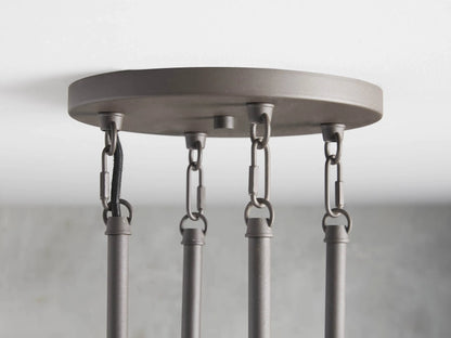 Round chandelier with 10 clear tubular glass shades, black steel frame, vertical rods; shown against a grey textured wall.