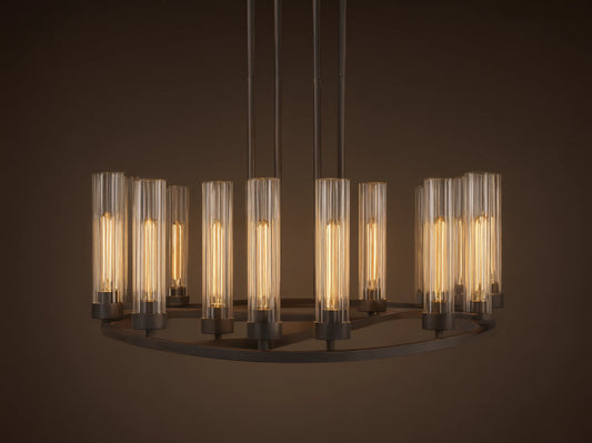 Andreas 10-Light Round Chandelier with a bronzed steel frame, featuring ten vertical, tubular clear glass shades. Mounted against a textured grey wall.