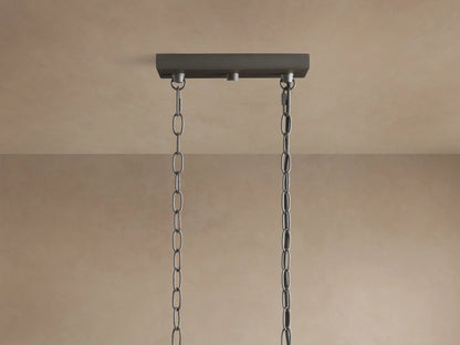 Close-up of Andreas Linear Chandelier: dark metal frame holding five ribbed clear glass shades with glowing Edison bulbs.