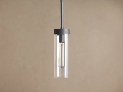 Andreas Pendant: Dark metal rod and cylindrical fixture holding a clear glass shade with a visible vintage filament bulb against a brown wall.
