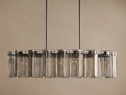 Delsie Oval Chandelier: Dark bronze steel frame with multiple clear fluted glass panels, suspended against a plain wall.